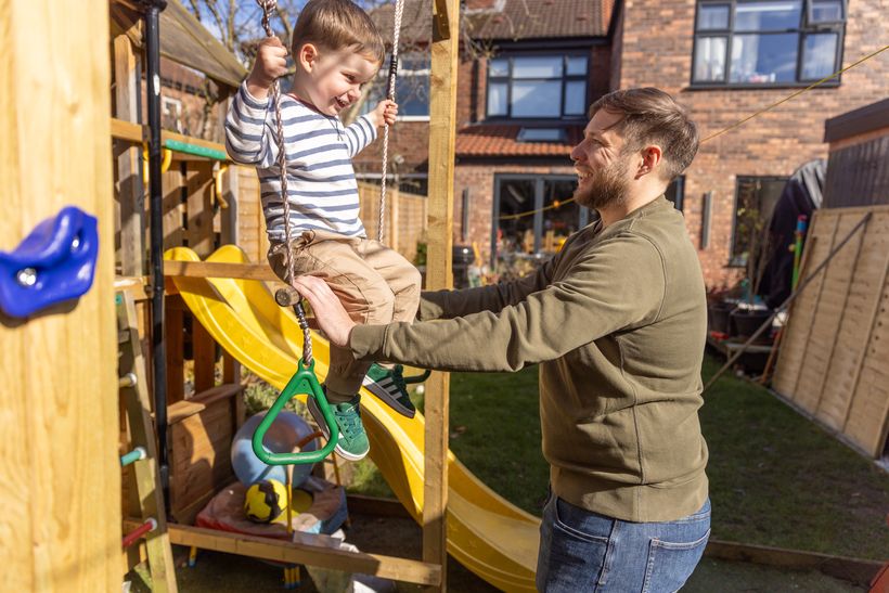 Craig pushing his son on a swing in the garden, both smiling