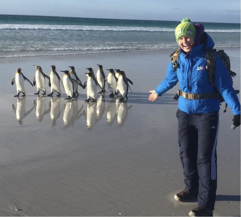 Beth stands on a beach near wild penguins