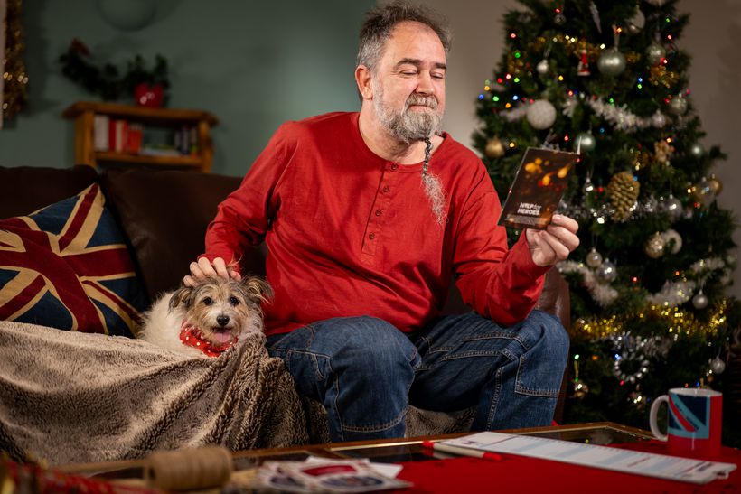 Mike sits with his dog, by a Christmas tree, reading a card