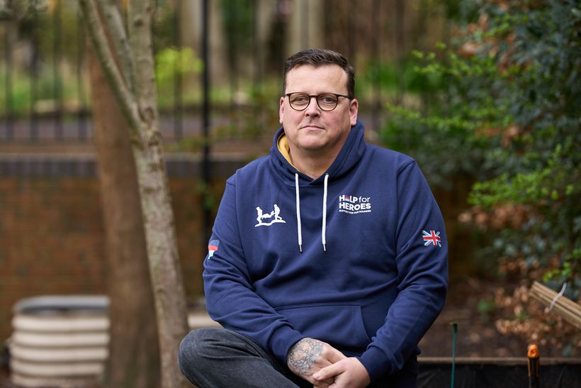 Veteran Lee sat on a wall staring into the camera. He wears a navy blue help for heroes hoody.