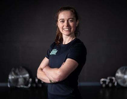 Alix, the instructor is smiling, with her arms crossed - against a dark background.