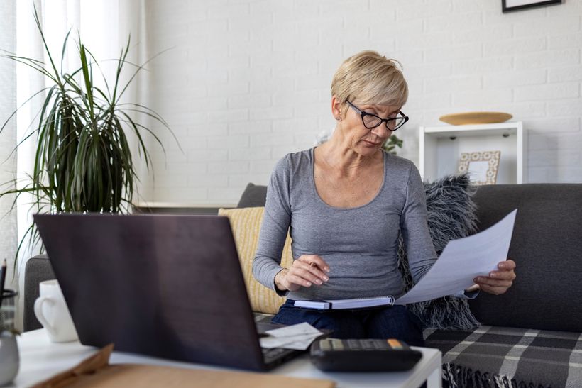 Middle aged woman looking at piece of paper with laptop in front