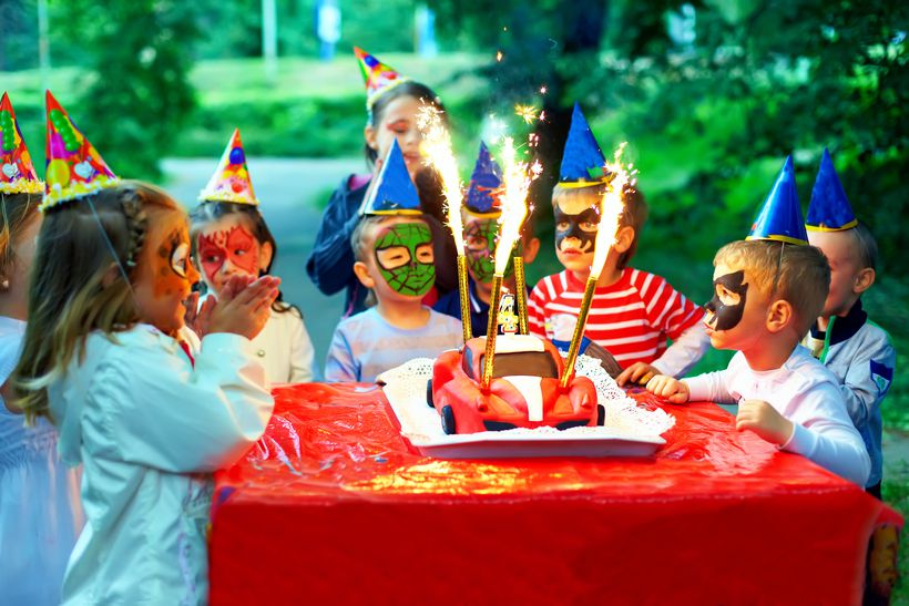 Children in party hats gather round a birthday cake with sparkle