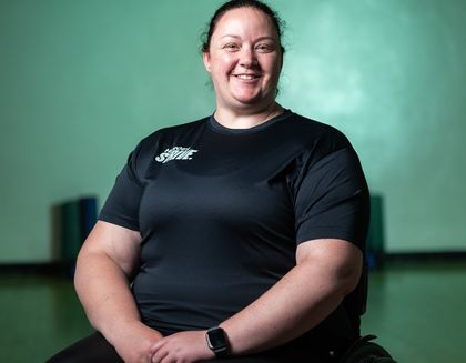 Gemma the instructor is smiling, sitting in a wheelchair - against a bright teal background.