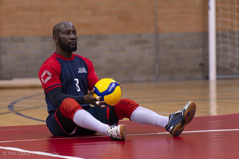 A man sat getting ready to serve in sitting volleyball game.
