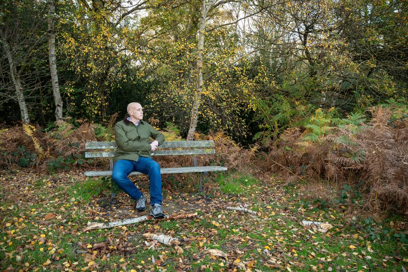A man sat on a bench looking to the side.