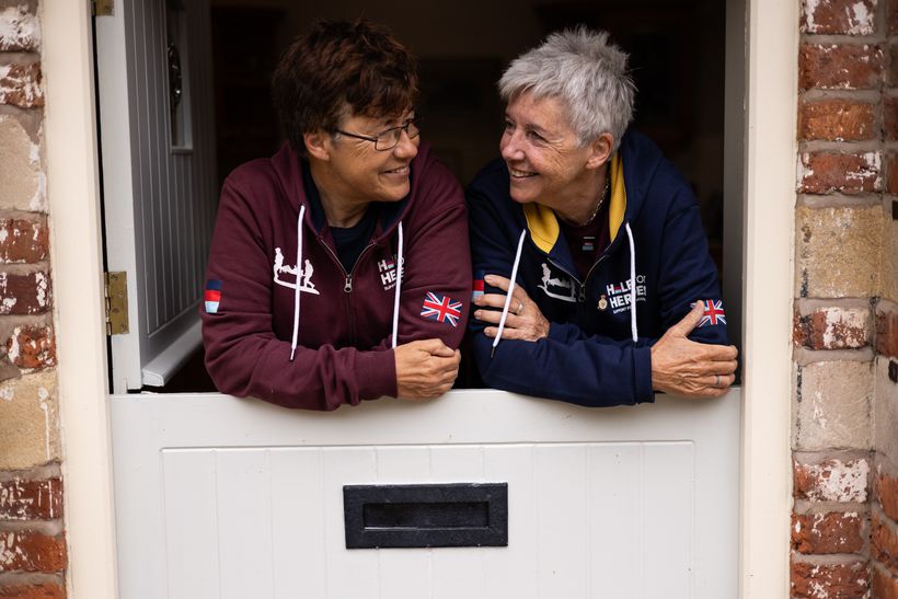 Jean and jo look at each other smiling in their front doorway