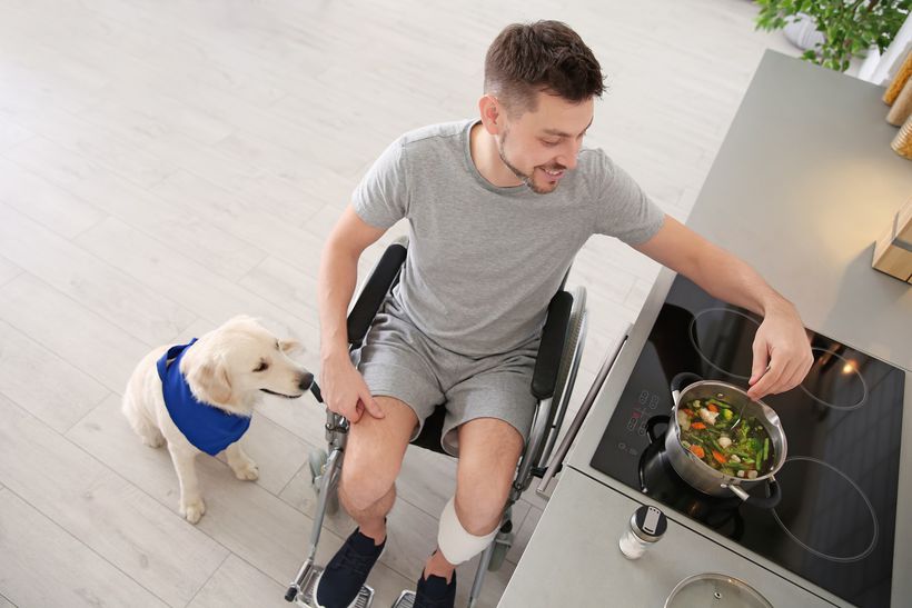 Young man in wheelchair cooking vegetables with dog next to him