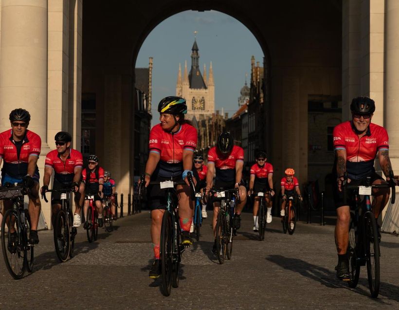 Group of cyclists riding beneath a large stone archway.