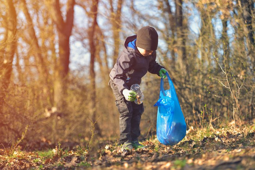 A child collects litter from a wooded area