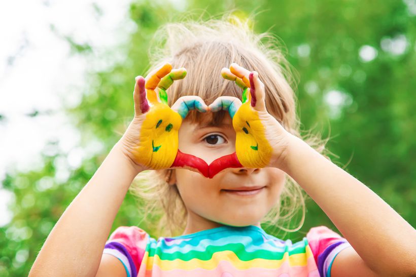 A child with hands covered in paint makes the shape of a love he