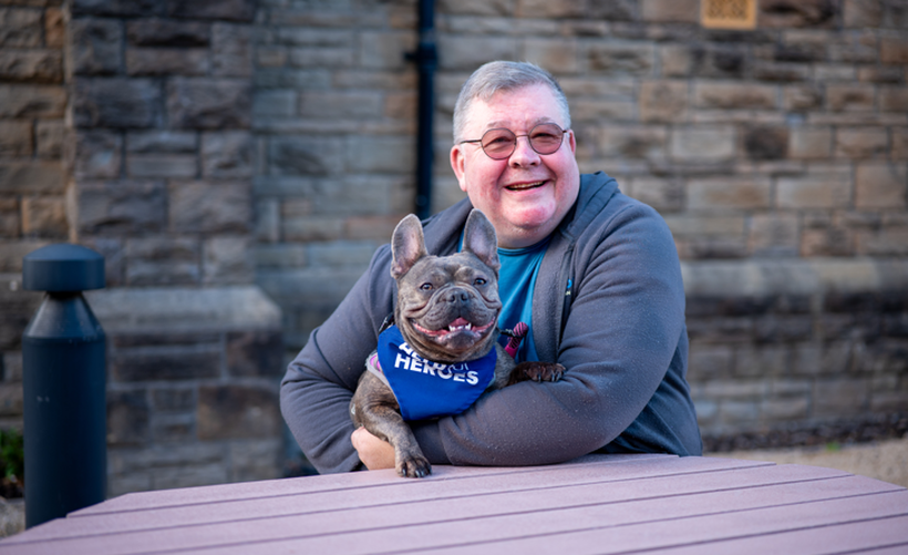 Paul and his dog sit smiling on a bench