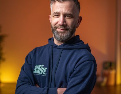 Paul the instructor is smiling, with his arms crossed - against a bright orange background.