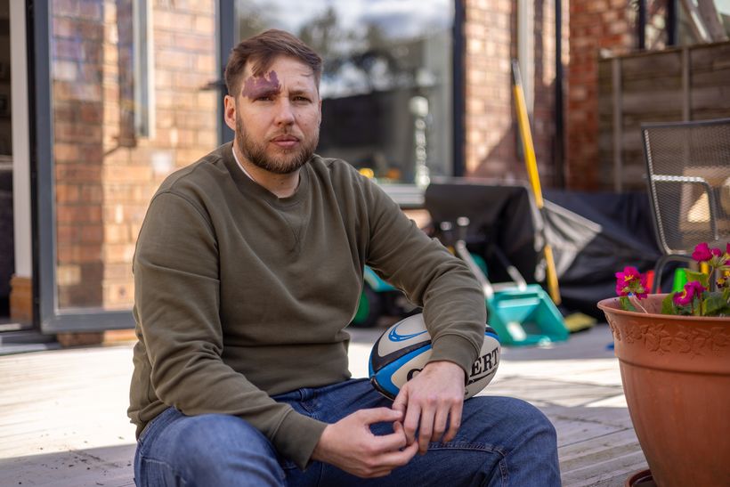 Craig sitting on his garden step holding a rugby ball