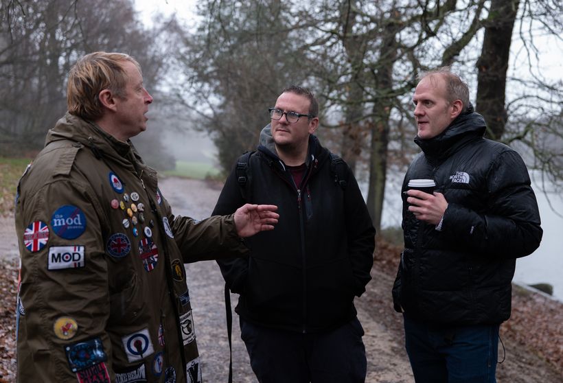 Three men are chatting outdoors on a grey day.