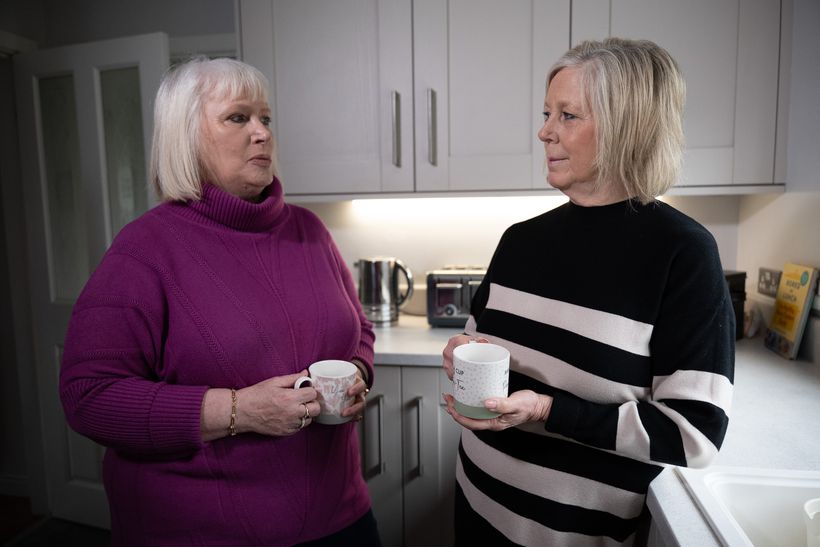 Two women with mugs of tea chatting in a kitchen.