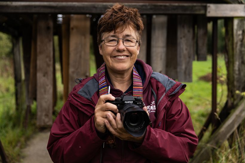 Jean stands holding a camera, looking happy
