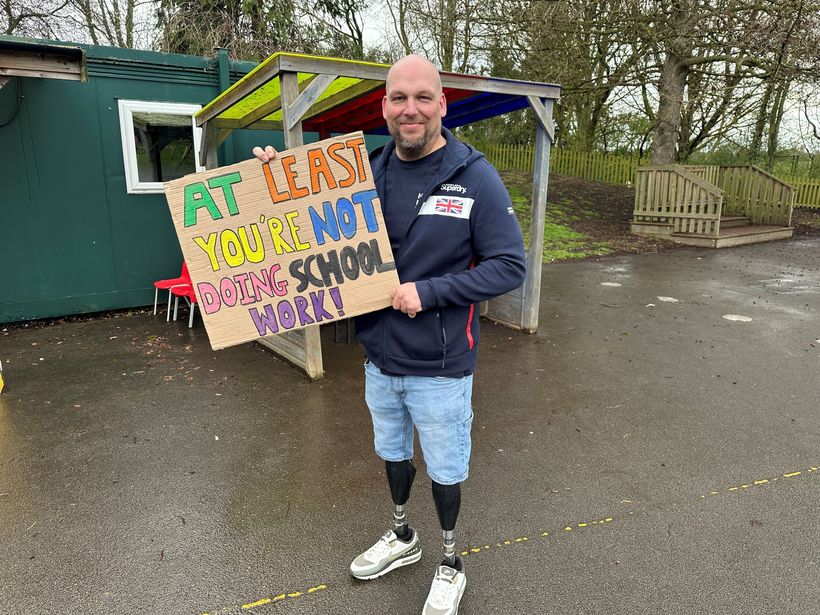 Image shows Tom holding a sign made by the pupils