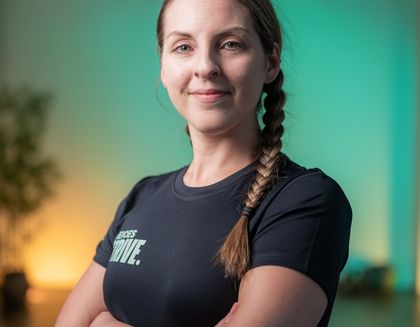 Kirsty the instructor is smiling, with her arms crossed - against a bright teal background.