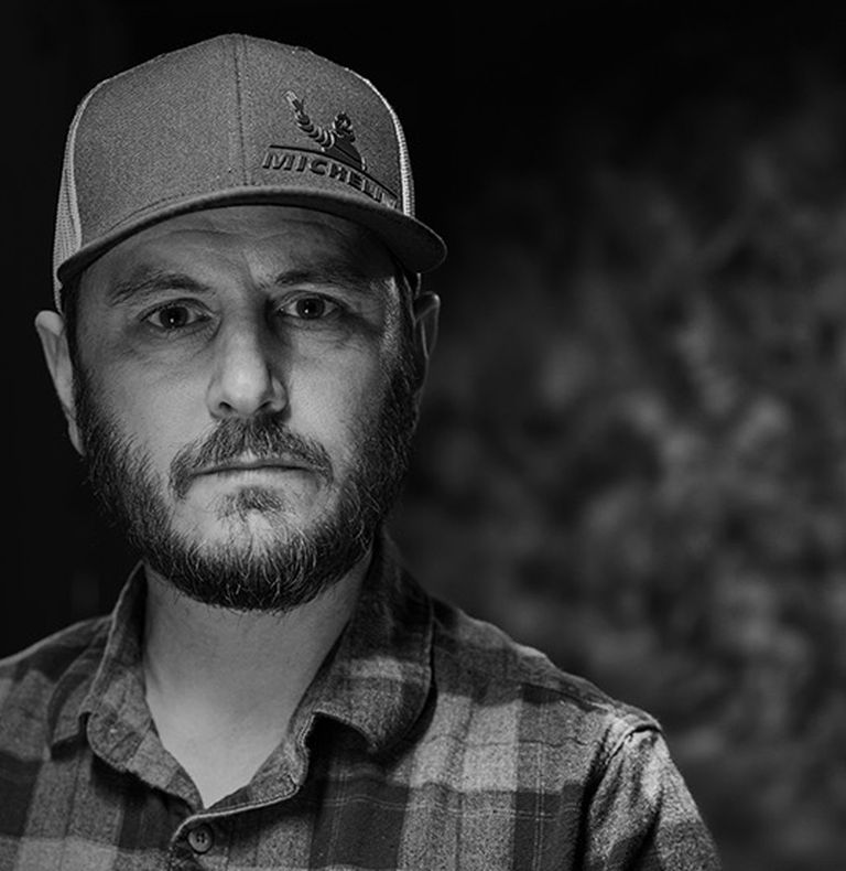 Veteran Chris to the right side of the image, staring straight at the camera. He is wearing a chequered shirt and a baseball cap.