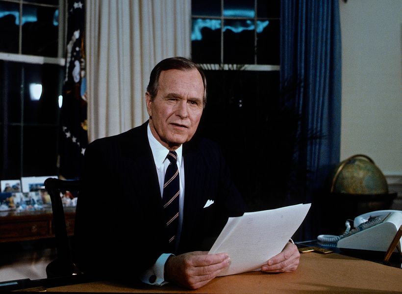 President Bush holding a piece of paper sat at a desk