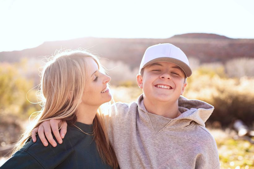 mother hugging teenage child both smiling in sunshine