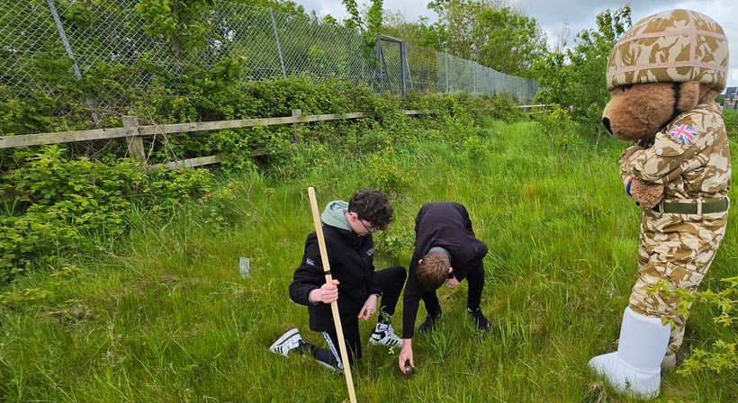 Two pupils planting a tree with Hero Bear watching