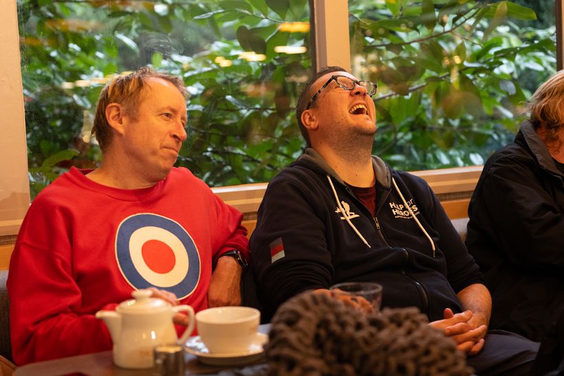 Two men are sat in a cafe and one of them is laughing.