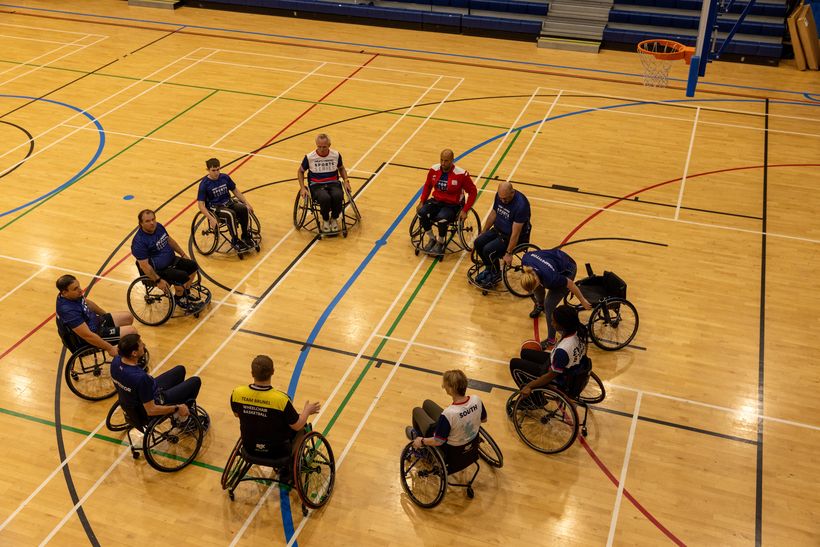 Group of people sat in wheelchairs in a circle in a sports hall
